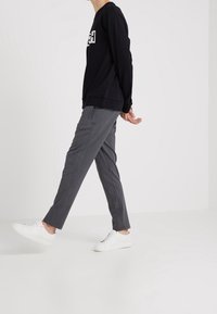 Black sweatshirt with white logo, grey slim-fit trousers with pinstriped texture, and white sneakers. Model walking in a neutral setting.