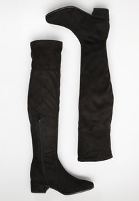 Schwarze Überknie-Stiefel aus weichem Wildleder-ähnlichem Material. Mit einem Reißverschluss an der Seite und einem niedrigen Blockabsatz. Glatte Textur und taillierter Schnitt.