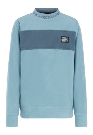 Personne portant un pull en polaire bleu avec une bande bleu foncé et un pantalon gris, debout devant un fond blanc.