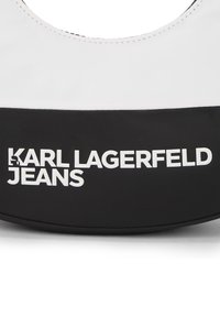 Juoda ir balta per petį nešama rankinė su lygiu paviršiumi, puikuojanti ryškiu "Karl Lagerfeld Jeans" prekės ženklu baltai ant juodos apatinės dalies.