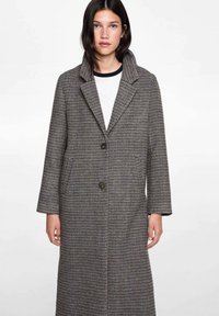 Long plaid coat made of textured fabric, featuring a shawl collar, two buttons, and side pockets. Colors include brown, black, and subtle white accents.