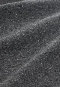 Gros plan d’un tissu en laine gris foncé avec une surface douce, texturée et légèrement duveteuse, présentant des plis doux et des fibres fines.