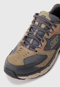 Tan and dark gray athletic shoe with a textured suede and mesh upper, featuring gray laces and orange accents on the sides and tongue.