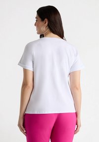 Hvid kortærmet top med opsmøg, glat tekstur, rund hals og en afslappet pasform, båret med pink underdele.