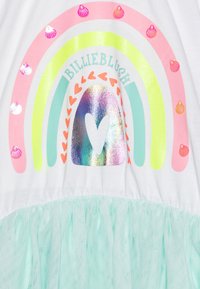 Biała koszulka z grafiką tęczy w odcieniach różu, żółci i zieleni, z metalicznymi i pastelowymi akcentami, zestawiona z miętową spódnicą z tiulu.