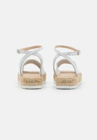 Bílé kožené espadrilky se strapci na kotníku, platformy obalené jutou a bílé gumové podrážky z pohledu zezadu.