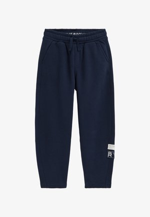 Marineblaue Jogginghose mit elastischem Bund, Kordelzug, Seitentaschen und zwei weißen und schwarzen Label-Patches am Unterschenkel.