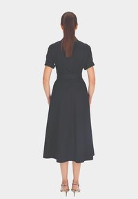 Czarna midi sukienka z krótkimi rękawami, wyraźnie zaznaczoną talią i rozszerzanym dołem; gładka tekstura, bez widocznych wzorów czy ozdób.