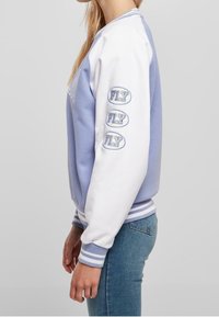 Světle modrá a bílá mikina s žebrovanými manžetami, s výšivkou "FLY" modře na levém rukávu. Měkký, neformální design z látky.