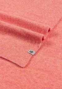 Soft pink wool fabric with a subtle texture, featuring a folded edge and a small label with black text on a beige background.