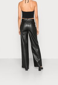 Pantalons larges en cuir noir avec taille haute, texture lisse et couture visible ; associés à un crop top noir ajusté.