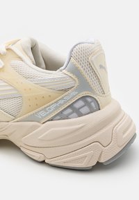 Puma Velophasis sneaker, krém és szürke hálós felsőrésszel, textúrált gumitalppal, fényvisszaverő részletekkel és márkázott elemekkel.