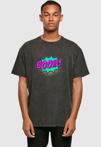 Zwarte spijker t-shirt met een losse pasvorm. Voorzien van een levendige comic-stijl "BOOM!" graphic in roze en turquoise op de borst. Korte mouwen.