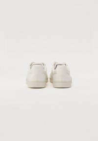 Sneakers in pelle bianca con una texture liscia, suola piatta e design minimalista. Presentano un logo sottile impresso sul tallone.