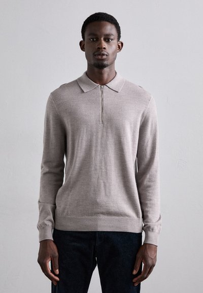 Pull en polo beige clair à manches longues avec un demi-zip, texture tricotée, et poignets côtelés. Assorti à un pantalon en denim foncé.