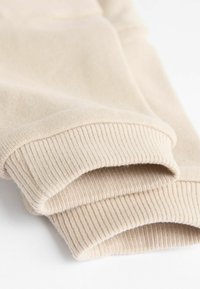 Beige színű pulóver mandzsetta, bordázott textúrával és sima felülettel. Puha anyag, amelyen a széleken látható varrási részletek találhatók.