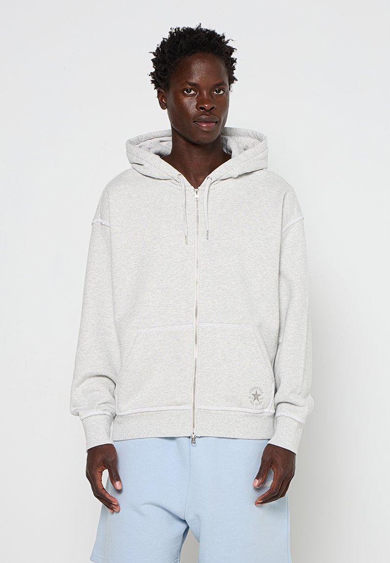 Hellgraue Zip-Hoodie mit einer Fronttasche, Kapuze mit Kordelzug und gerippten Bündchen. Der Stoff wirkt weich mit dezentem Muster.