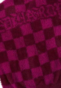 Chundelatý pléd v kostkovaném vzoru s střídajícími se čtverci tmavě magentové a tmavě burgundské barvy. Měkká textura po celém povrchu.