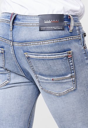 Šviesiai mėlynos džinsinės kelnės su pritaikytu dizainu, kontrastinga siuvimo linija, dviem užpakalinėm kišenėm ir prekės ženklu ant liemens.