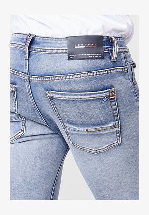 Heledad sinine teksapüksid, millel on vormitud disain, kontrastõmblused, kaks tagataskut ja brändi silt vööl.