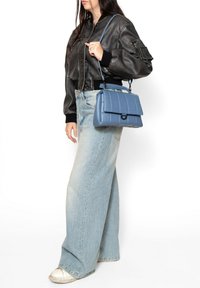 Borsa a tracolla trapuntata di colore blu chiaro con soffietto superiore, manico corto e tracolla removibile. Abbinata a una giacca in pelle nera corta e jeans a gamba larga.