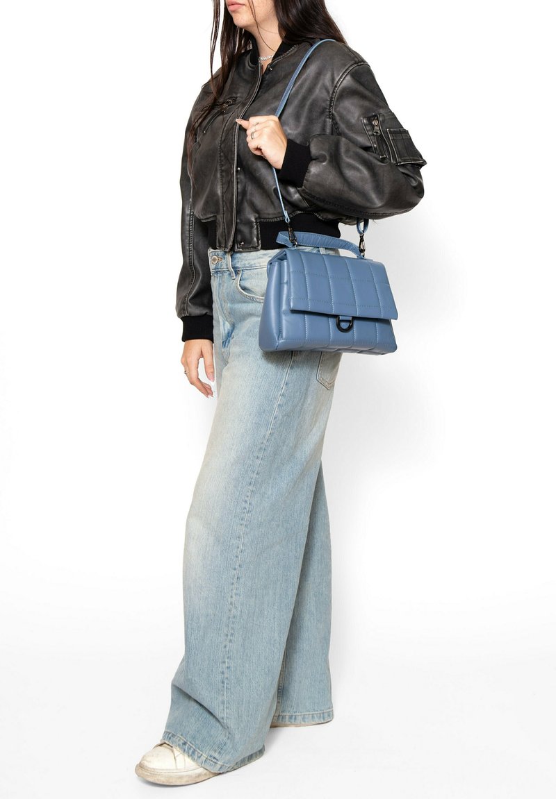 Borsa a tracolla trapuntata di colore blu chiaro con soffietto superiore, manico corto e tracolla removibile. Abbinata a una giacca in pelle nera corta e jeans a gamba larga.