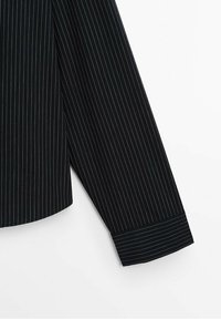 Partie de chemise noire à manches longues avec fines rayures blanches verticales et détail des poignets sur un fond blanc uni.