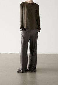 Blouse vert olive à manches longues avec un col rond et trois boutons. Associée à un pantalon large en satin gris charbon, texture lisse.