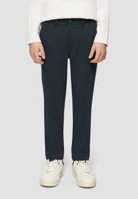 Donker marineblauwe, slim-fit broek van subtiel gestructureerde stof, met een knoopsluiting en standaard riemlussen, gecombineerd met witte sneakers.