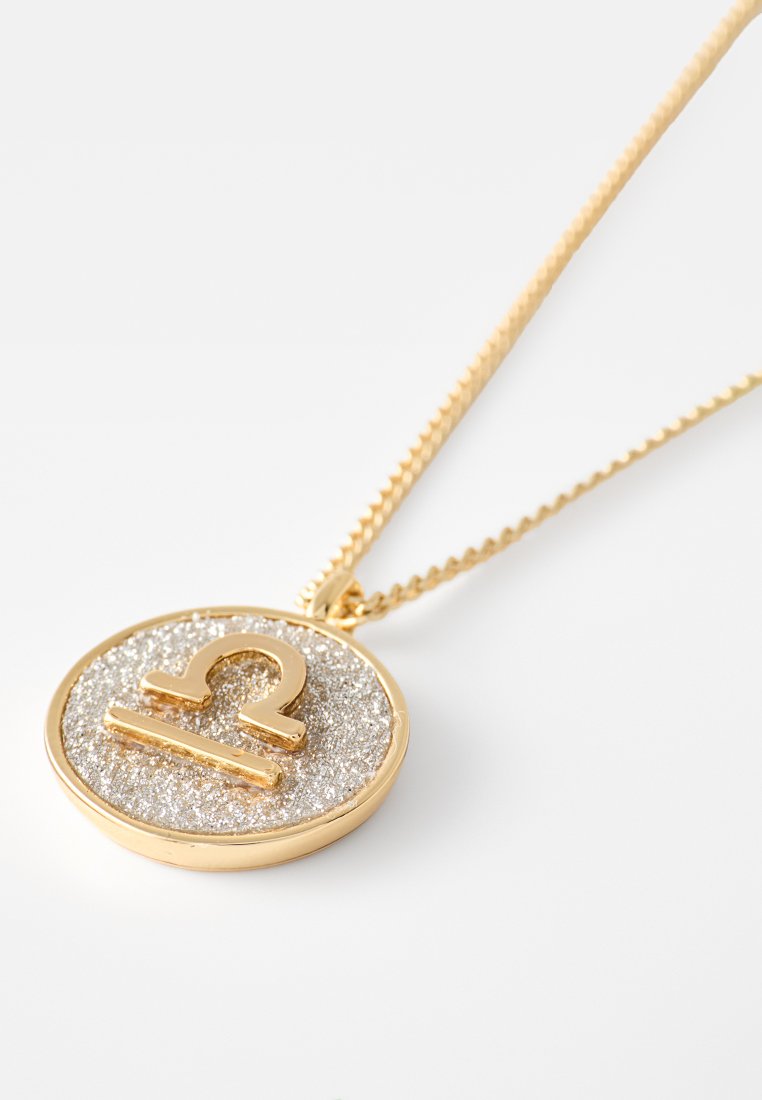 Halskette in Goldton mit einem runden Anhänger. Der Anhänger hat eine strukturierte silberne Oberfläche mit einem erhabenen goldenen Tierkreiszeichen. Detaillierte Kettenglieder.