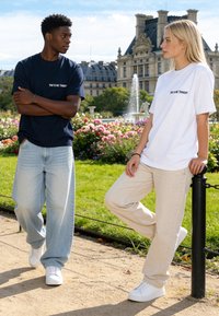 Jeune homme et femme portant des t-shirts assortis « YOU & ME TONIGHT », debout et penchés dans un parc avec des fleurs et une fontaine derrière eux.