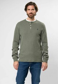 Zöld, hosszúujjú henley ing, texturált mintával, három gombos nyakkivágással és kis logóval a bal mellrészen, farmernadrággal párosítva.