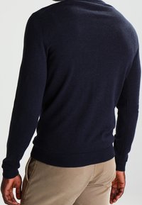 Marinblå stickad tröja med långa ärmar och ribbade muddar och nederkant. Mjuk textur och figurnära design, sedd bakifrån.