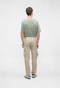 Pantalones cargo color caqui con bolsillos laterales, combinados con una camisa de manga corta texturizada de color verde claro. El calzado presenta un diseño en negro y gris.