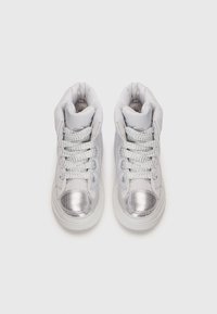 Zapatillas altas plateadas con collar acolchado, punta de malla y cordones trenzados sobre un fondo blanco. Material superior sintético suave.