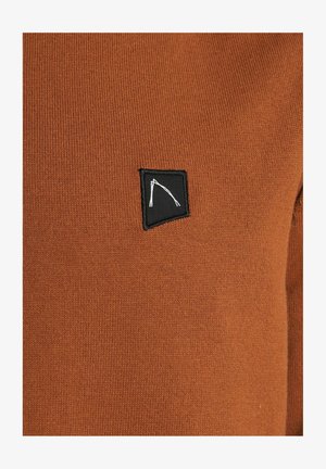 Rudi spalvos megztinis su tekstūru ir nedidele juoda logotipo etikete, prasiskverbiančia baltais akcentais.