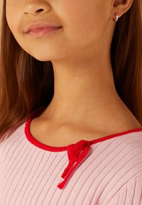 Hellrosa geripptes Oberteil mit rotem Ausschnitt und Kordelzugdetails. Die glatte Textur und das taillierte Design betonen das legere Erscheinungsbild.