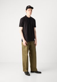 Čierna polokošeľa s krátkymi rukávmi, olivovo zelené nohavice a čierne topánky. K outfitu sa hodí čierny šiltovka s logom "BOSS" v zlatej farbe.
