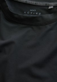 Schwarzes Sportshirt mit rundem Ausschnitt und glatter Textur. "NEXT ACTIVE" auf dem inneren Halsausschnitt aufgedruckt. Haltbare Nähte sichtbar.