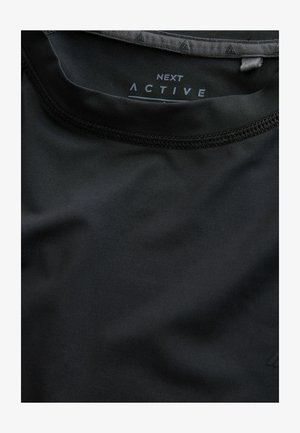 Mustast aktiivrõivast särgist, millel on ümar kaelus ja sile pind. Kaeluse siseküljel on trükitud "NEXT ACTIVE". Näha on vastupidav õmblus.