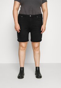 Shorts de mezclilla negra con dobladillo enrollado, con bolsillos frontales y cierre de botón, combinados con botas negras hasta el tobillo y una camiseta gris.