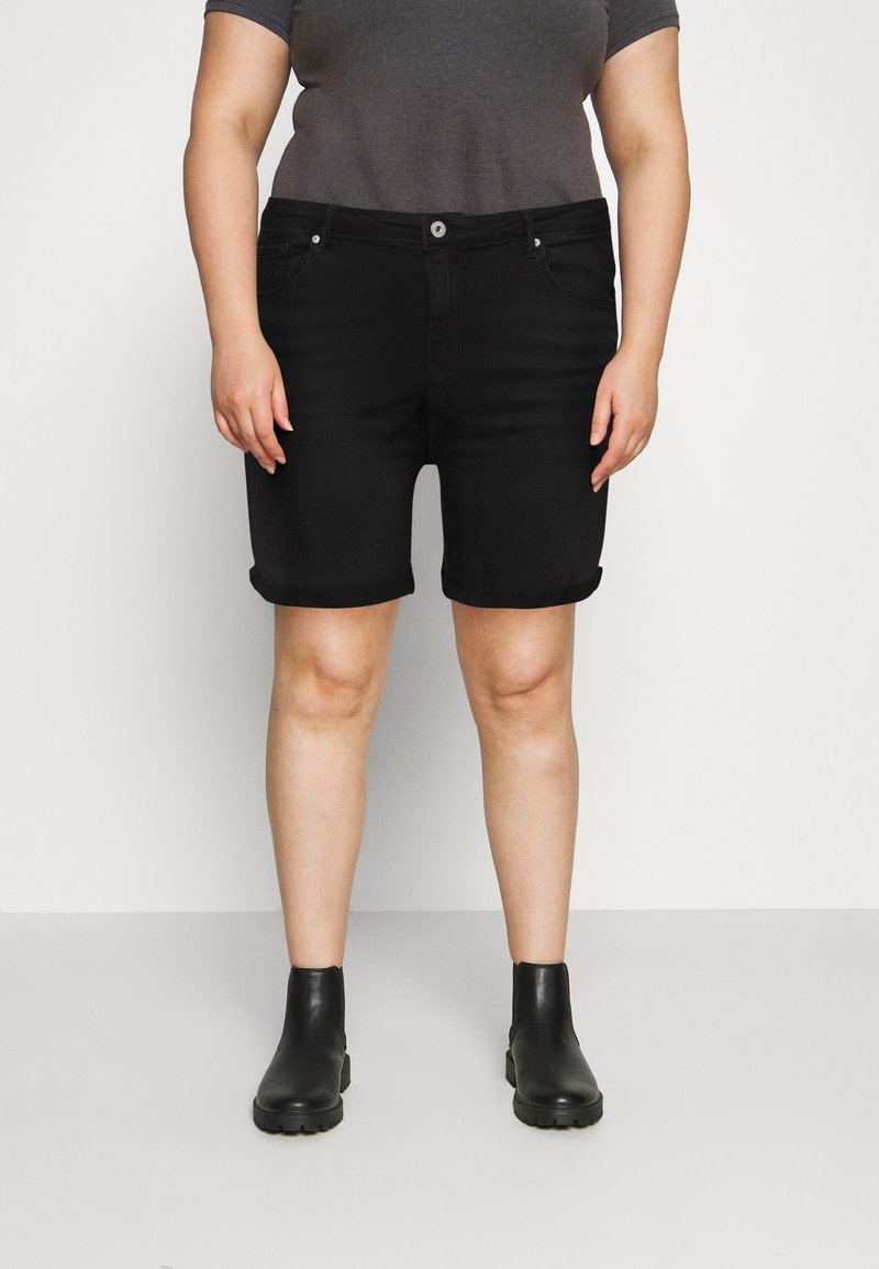 Shorts de mezclilla negra con dobladillo enrollado, con bolsillos frontales y cierre de botón, combinados con botas negras hasta el tobillo y una camiseta gris.