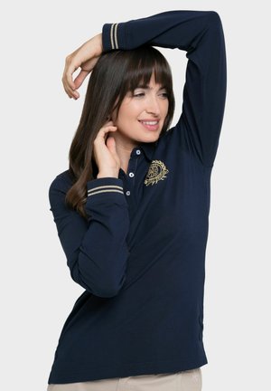Polo de manga larga azul marino con un logo bordado en dorado y puños a rayas. Fabricado en una tela suave, con un corte clásico y tapeta de botones.