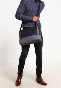 Svart och grå messenger-väska med Calvin Klein-logotyp, rektangulär form, justerbar rem, tillverkad av slitstarkt material, slät yta.