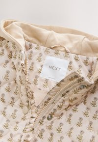 Veste légèrement matelassée avec un motif floral aux tons beige et or. Dotée d'une fermeture éclair, d'une doublure côtelée et d'une étiquette de la marque NEXT.