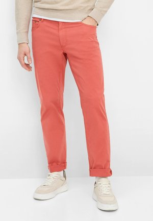 Herre bomuldsbukser i koral med en slank pasform, der har et klassisk design med fem lommer, op rullede manchetter og kombineret med beige sneakers.