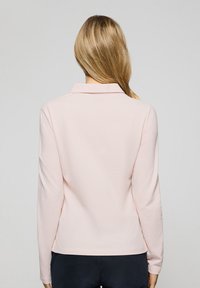 Ljusrosa långärmad polo-tröja med krage, slät tyg, figursydd design och en lätt böjd fåll bak.