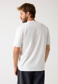 T-shirt bianco a maniche corte realizzato in cotone morbido. Presenta un classico colletto a girocollo e una vestibilità comoda, con una texture liscia e un design semplice.