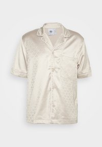 Satin skjorta med kort ärm i ljusbeige, med ett subtilt bladmönster, kantad med vit piping, med en enda bröstficka och knappar.