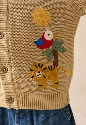 Beige gestrickte Strickjacke mit Knopfverschluss, mit gestickter Sonnenblume, rotem und blauem Vogel auf Palme und gelbem Tiger-Patch.